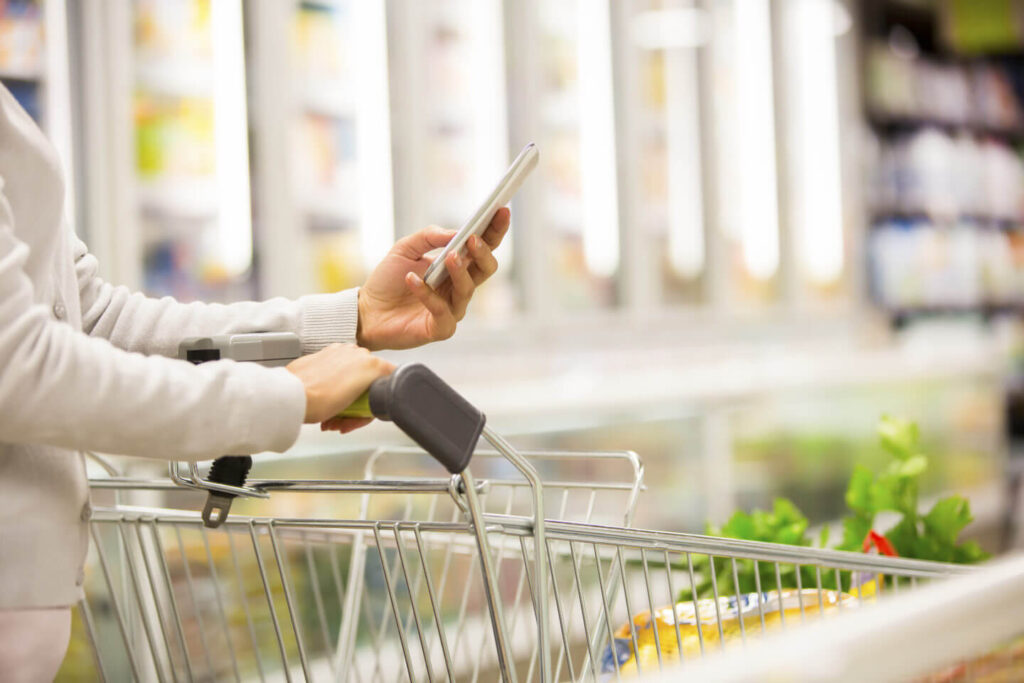 187535881 woman using mobile phone while shopping in supermarket 1440x960 1 1